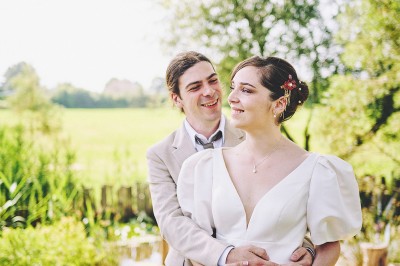 Un couple de mariés s'embrasse tendrement près d'un étang, entouré de verdure, la mariée tenant un bouquet coloré.