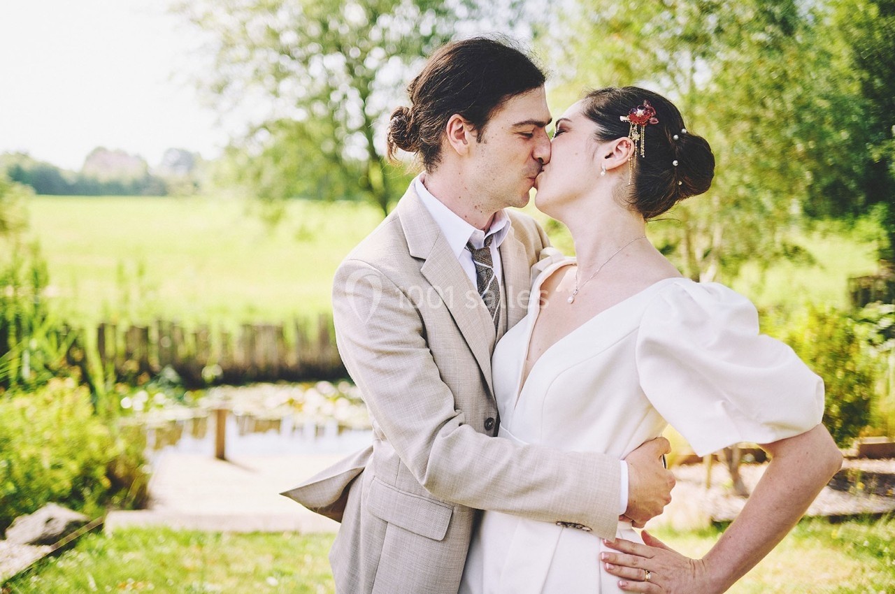 Un couple en tenue de mariage s'embrasse tendrement dans un jardin verdoyant près d'un étang.