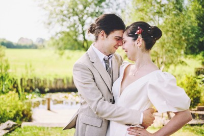 Un couple de mariés s'embrasse tendrement près d'un étang, entouré de verdure, la mariée tenant un bouquet coloré.