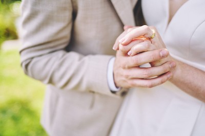 Un couple de mariés s'embrasse tendrement près d'un étang, entouré de verdure, la mariée tenant un bouquet coloré.