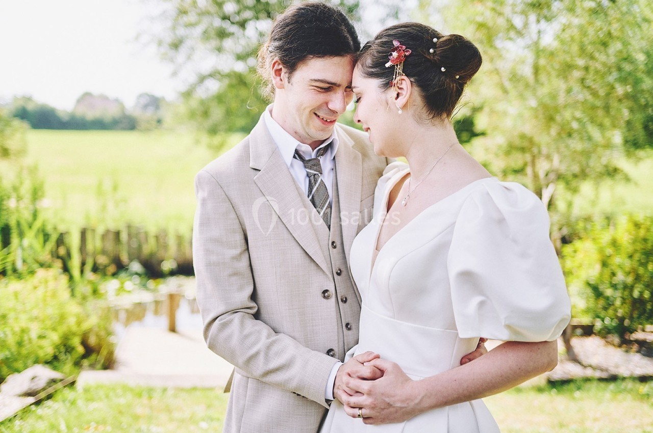 Un couple en tenue de mariage se tient tendrement dans un jardin verdoyant par une journée ensoleillée.