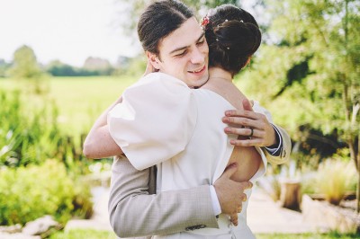 Un couple de mariés s'embrasse tendrement près d'un étang, entouré de verdure, la mariée tenant un bouquet coloré.