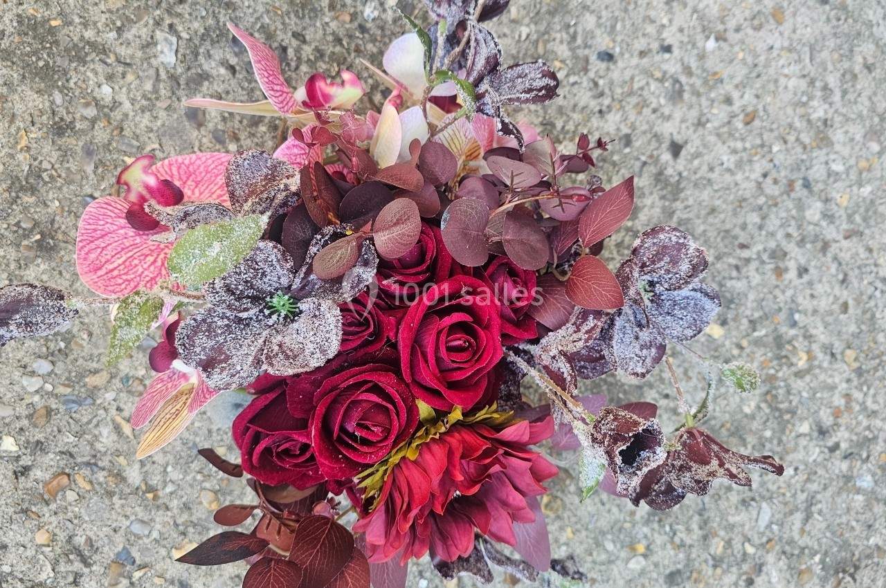 Bouquet de fleurs rouges et violettes avec feuillage givré, posé sur un sol en béton gris.