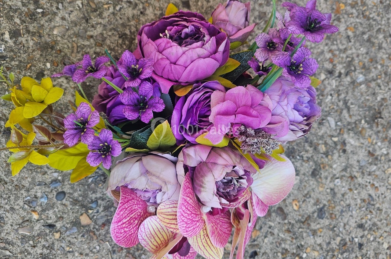 Bouquet de fleurs violettes et roses avec des touches de jaune, posé sur un sol en béton.