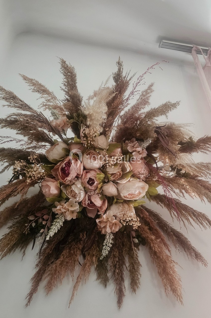 Composition florale suspendue avec des fleurs séchées et des pampas dans des tons neutres et rosés.