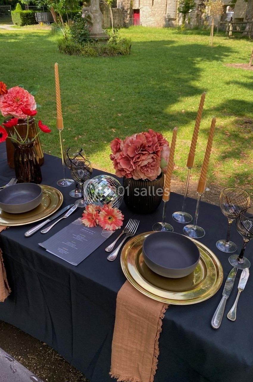 Table élégamment dressée en extérieur avec vaisselle noire, bougies torsadées, fleurs colorées et boule à facettes.