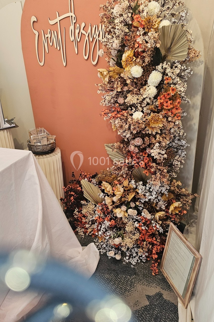 Mur décoratif avec fleurs séchées et fraîches dans des tons chauds, accompagné d'une inscription ’Event Design’.