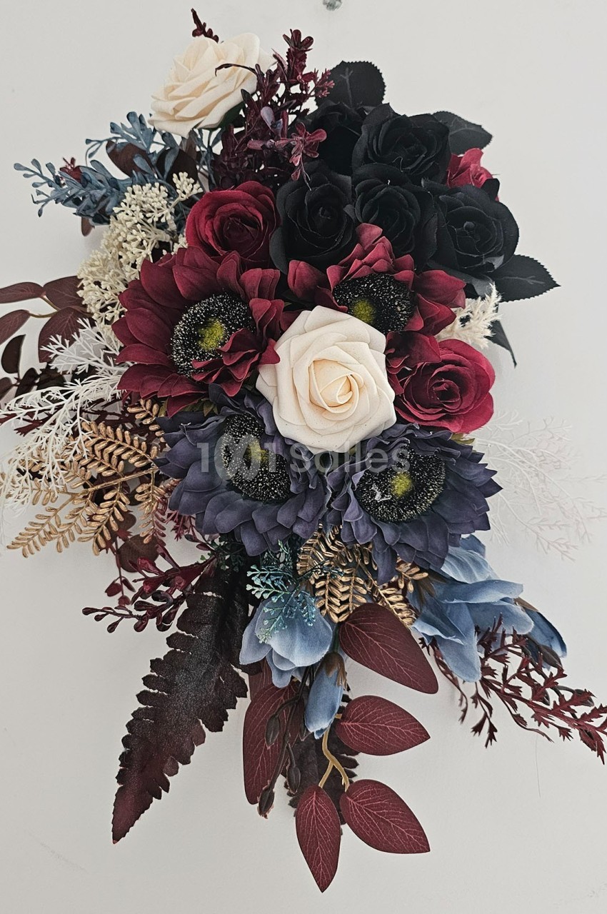Arrangement floral avec des roses rouges, blanches et noires, des fleurs bleues et des feuillages variés sur fond clair.