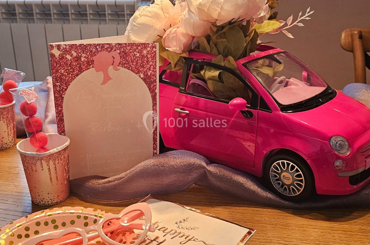 Une petite voiture rose utilisée comme vase avec des fleurs, entourée de décorations d'anniversaire sur une table.