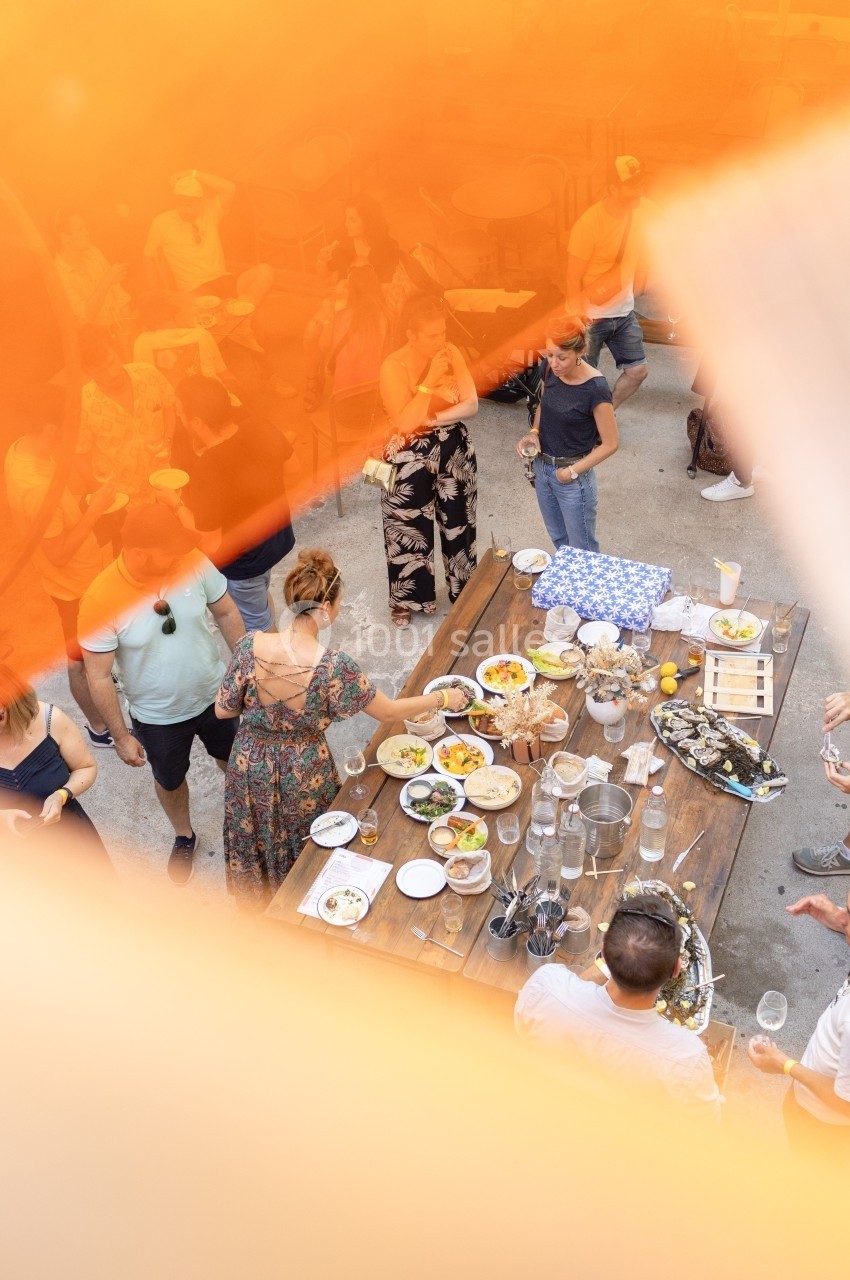 Vue plongeante sur une table garnie de plats variés entourée de personnes lors d'un repas en extérieur.