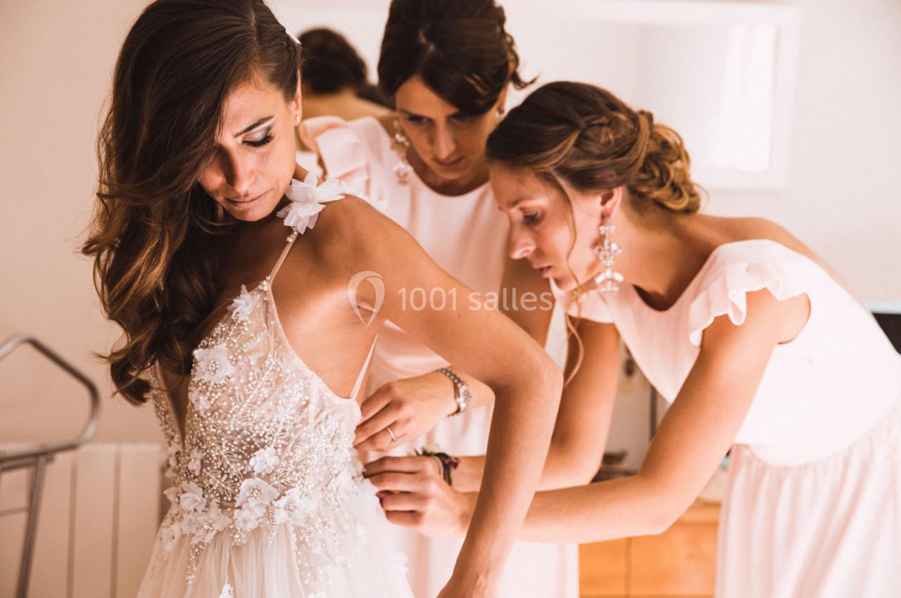 Deux femmes ajustent la robe de mariée d'une troisième femme dans une pièce lumineuse.