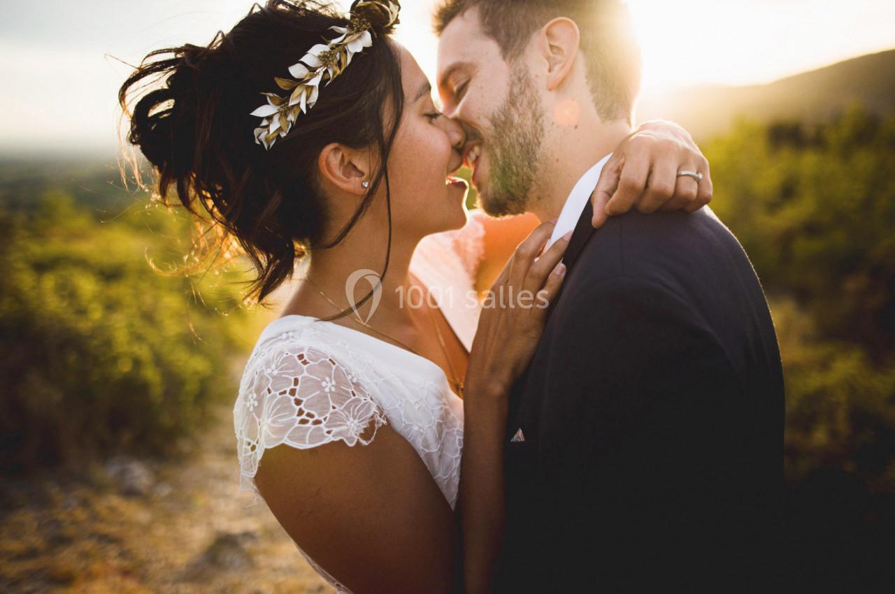 Un couple en tenue de mariage s'embrasse tendrement en extérieur au coucher du soleil.
