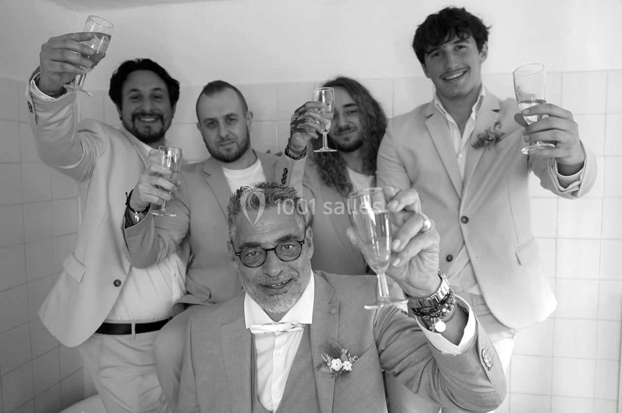 Cinq hommes en costume clair, souriants, levant leurs verres dans un geste de célébration dans une pièce lumineuse.