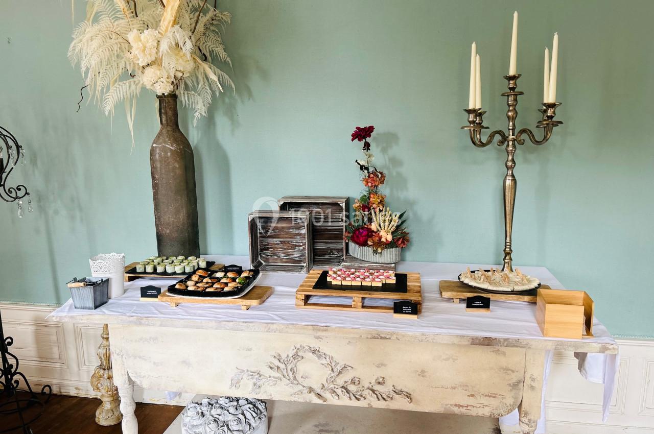 Table décorée avec des desserts variés, des fleurs séchées et des bougies dans un chandelier, sur fond de mur vert.