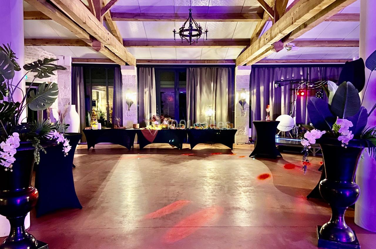 Salle de réception décorée avec des plantes, des tables drapées de noir et un éclairage tamisé coloré.