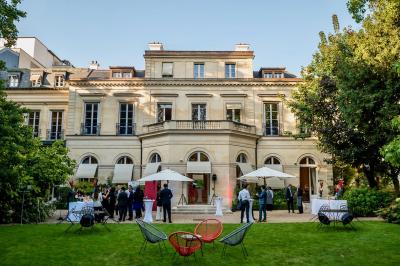 Miniature Traiteur Saint-Cloud (Hauts-de-Seine) - Aux Jardins des Sens #39 Façade illuminée d'un bâtiment élégant au crépuscule, avec un jardin et des invités rassemblés devant.
