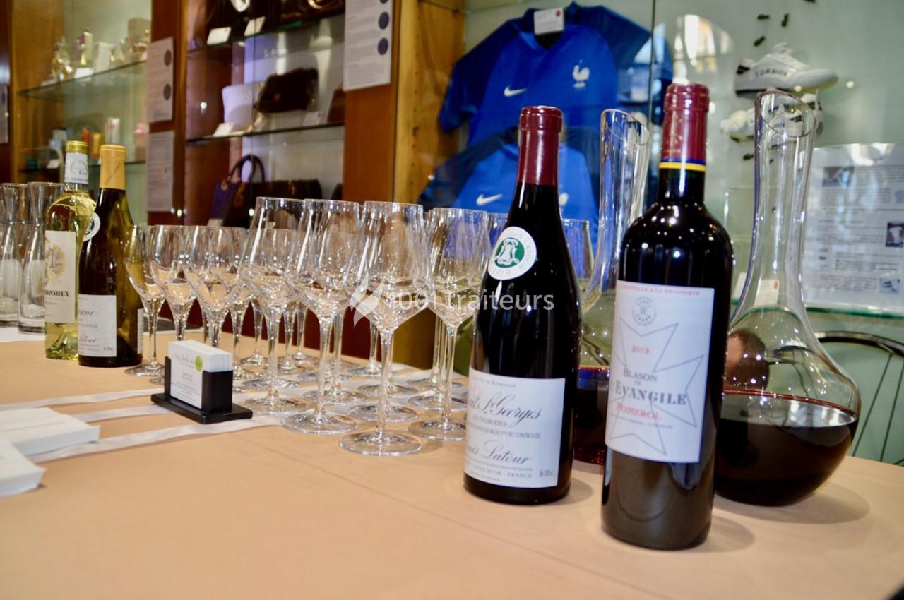 Bouteilles de vin rouge et blanc avec verres à vin alignés sur une table, devant une vitrine d'objets divers.