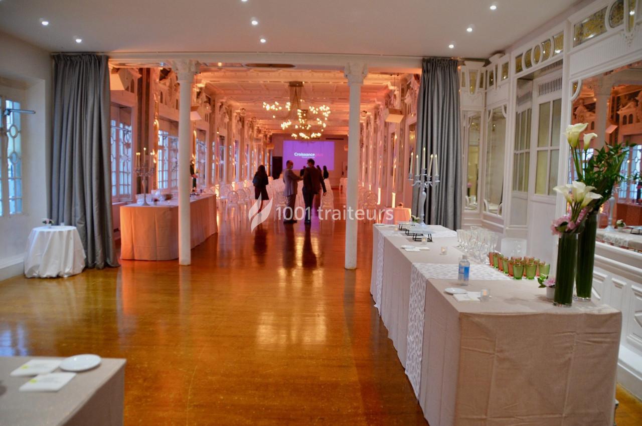 Salle élégante avec décor lumineux, tables dressées pour un événement, et quelques personnes en arrière-plan.