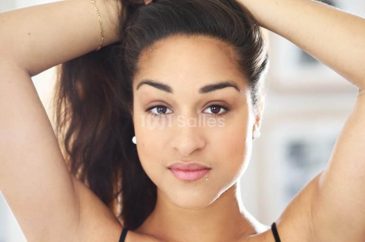 Femme aux cheveux attachés regardant l'objectif, éclairage naturel et arrière-plan flou.