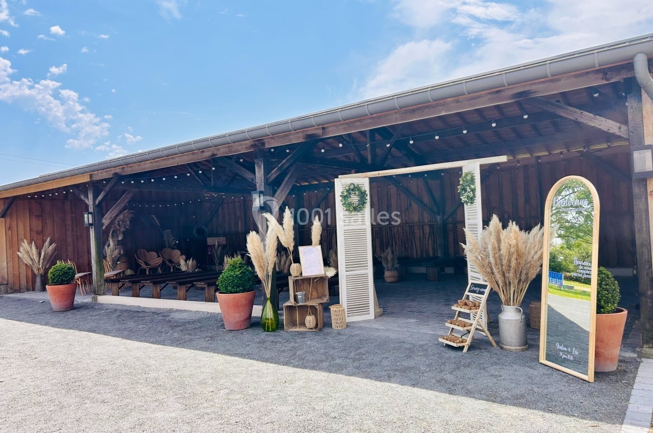 Entrée d'une grange aménagée pour un événement, décorée avec des plantes, des panneaux en bois et des herbes de la pampa.