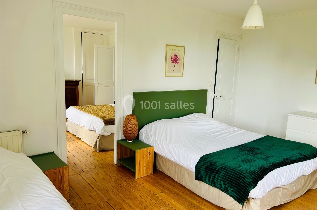 Chambre lumineuse avec parquet, deux lits simples, linge de lit blanc et décoration minimaliste.
