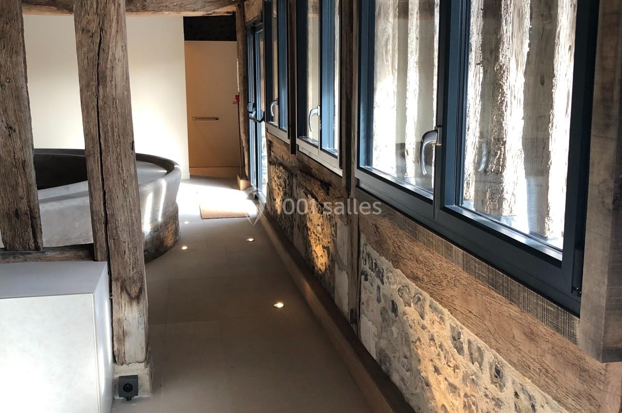 Couloir lumineux avec murs en pierre et poutres en bois apparentes, éclairé par des spots au sol et des fenêtres modernes.
