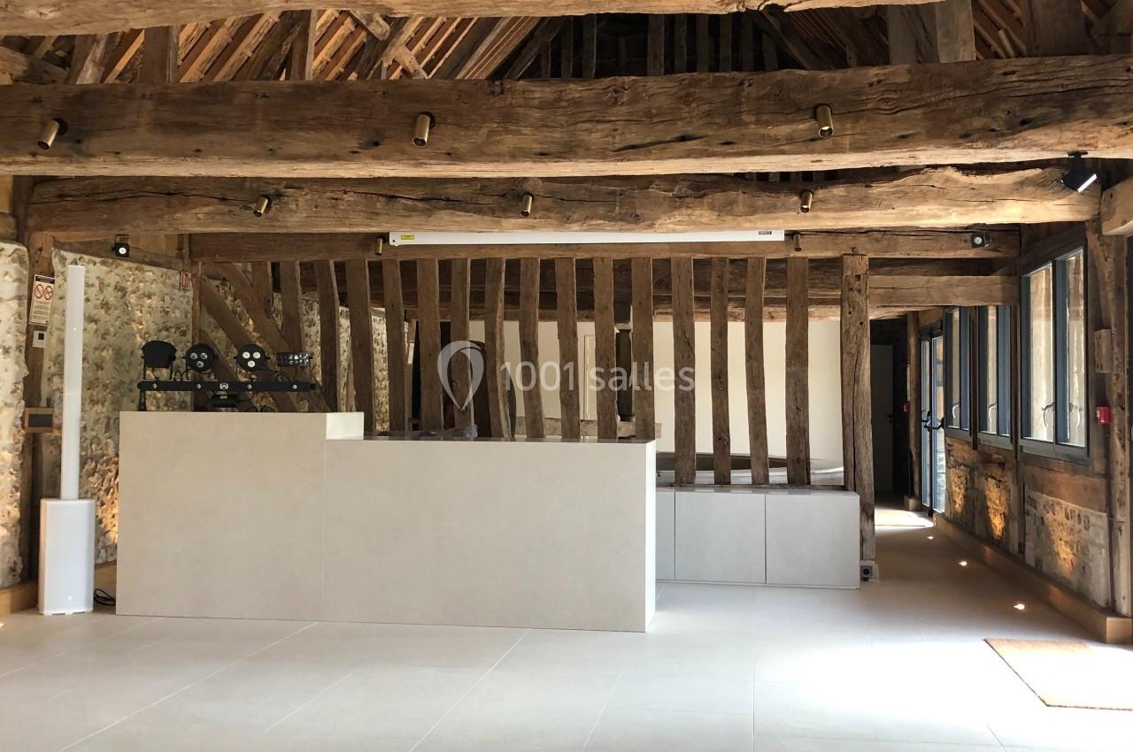 Intérieur d'une salle rénovée avec poutres en bois apparentes, murs en pierre et comptoir moderne au centre.