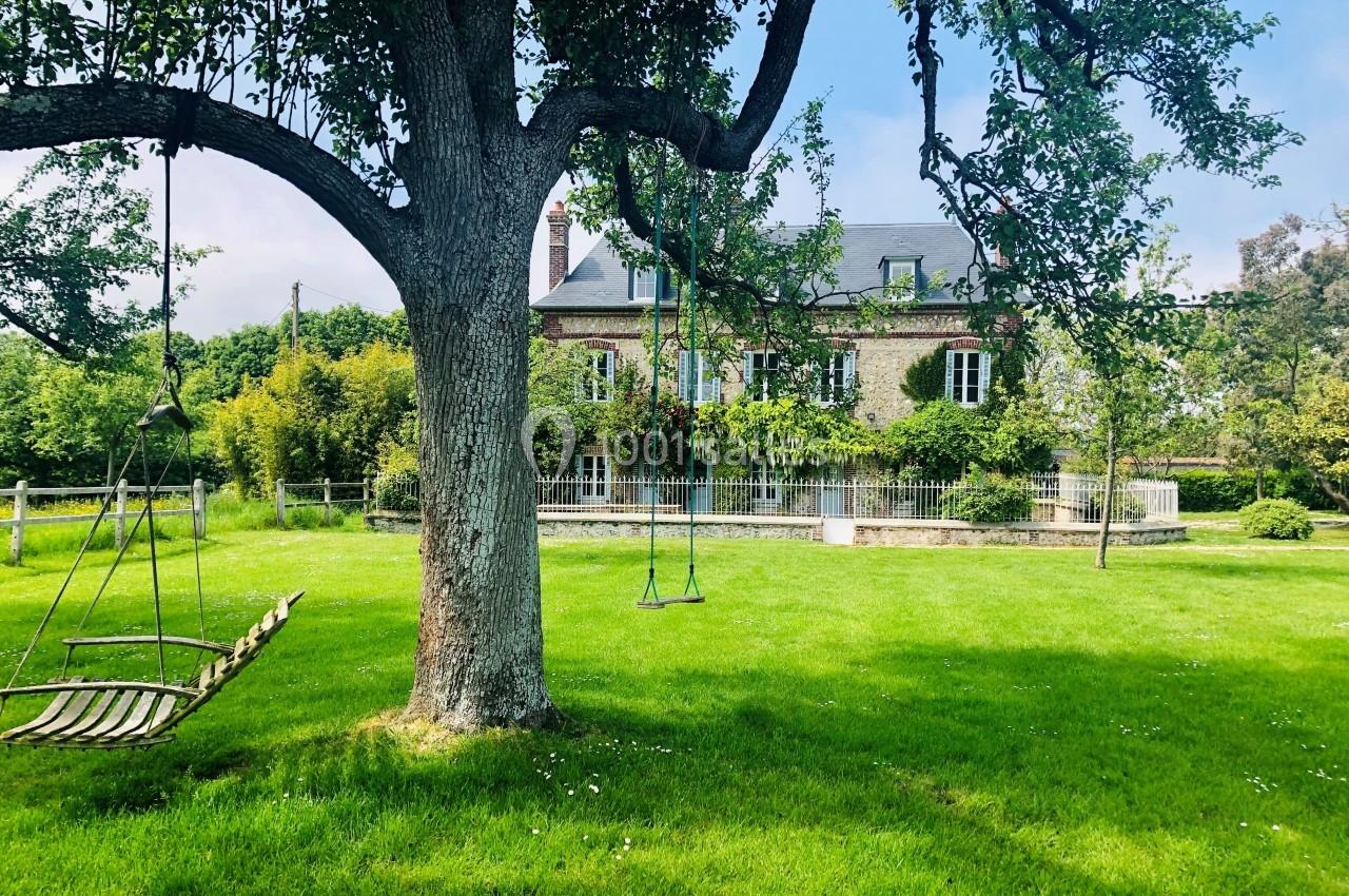 Maison en pierre entourée d'un grand jardin verdoyant avec une balançoire suspendue à un arbre.