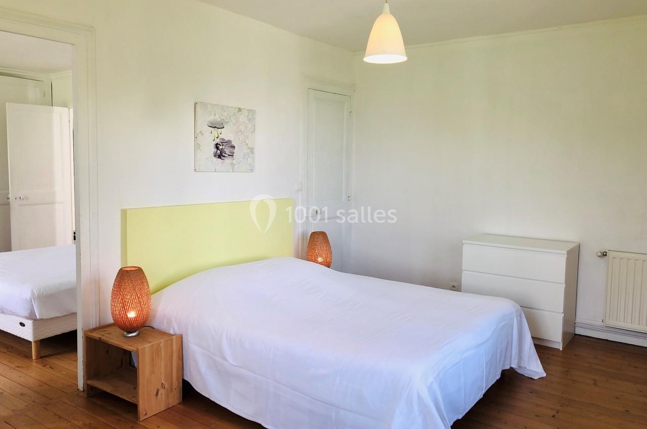 Chambre lumineuse avec lit double, lampes de chevet, commode blanche et parquet en bois clair.