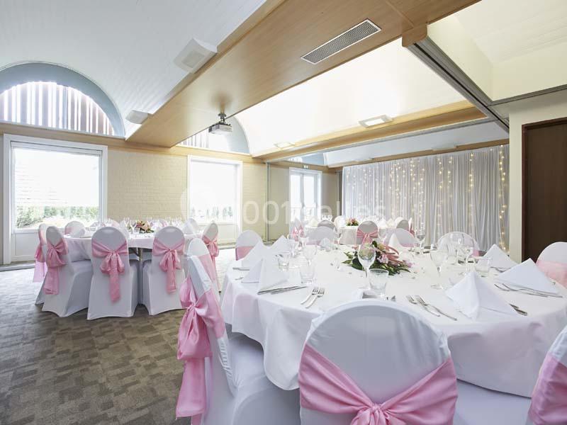 Location salle Noyelles-Godault (Pas-de-Calais) - Novotel Lens Noyelles #6 Salle de réception décorée avec des tables rondes, nappes blanches, chaises ornées de nœuds roses et rideaux lumineux.