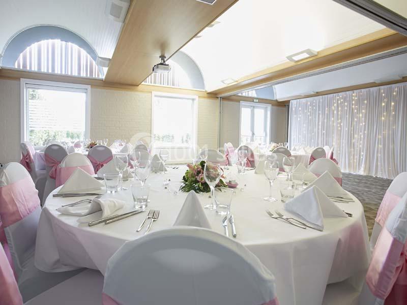 Location salle Noyelles-Godault (Pas-de-Calais) - Novotel Lens Noyelles #8 Salle de réception décorée avec des tables rondes, nappes blanches, serviettes pliées et chaises ornées de rubans roses.