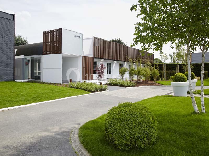 Location salle Noyelles-Godault (Pas-de-Calais) - Novotel Lens Noyelles #2 Bâtiment moderne entouré de pelouses bien entretenues, d'arbres et de grands pots de fleurs blanches.