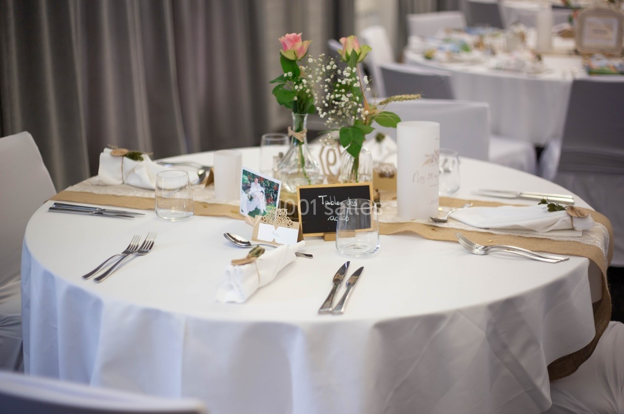 Location salle Noyelles-Godault (Pas-de-Calais) - Novotel Lens Noyelles #13 Table ronde décorée pour un événement, avec nappe blanche, fleurs, bougies et marque-place sur une bande en toile de jute.