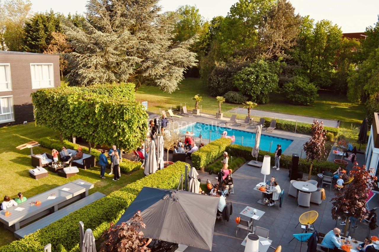 Location salle Noyelles-Godault (Pas-de-Calais) - Novotel Lens Noyelles #1 Vue aérienne d'une terrasse animée avec des tables, des parasols et une piscine entourée de verdure.
