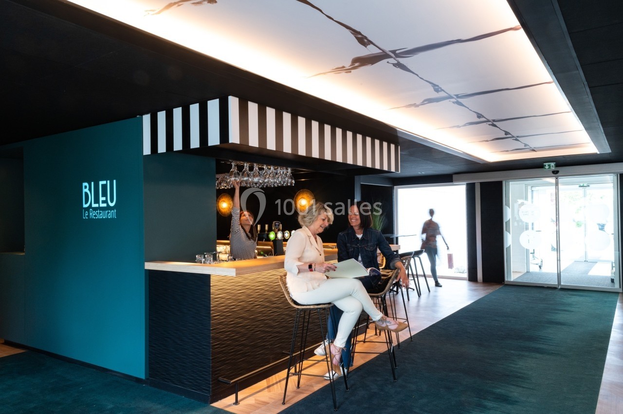 Location salle Noyelles-Godault (Pas-de-Calais) - Novotel Lens Noyelles #20 Deux femmes assises au bar d'un restaurant moderne avec un barman en arrière-plan.