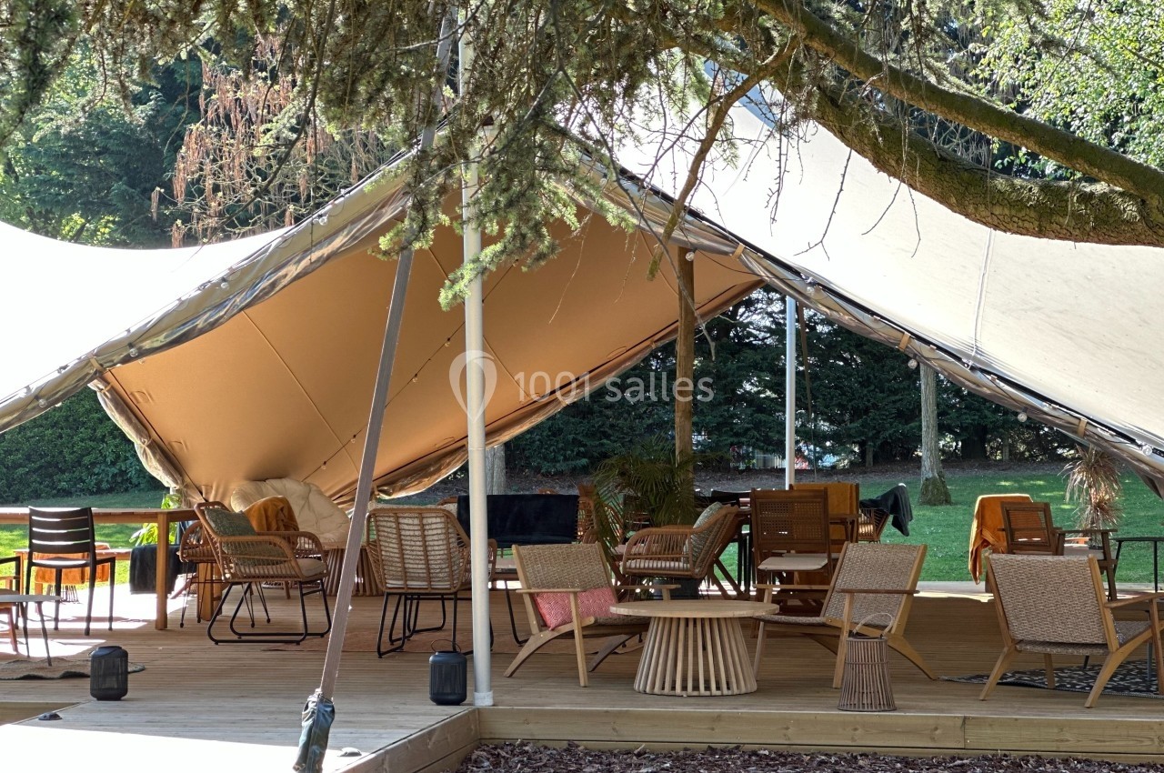 Location salle Noyelles-Godault (Pas-de-Calais) - Novotel Lens Noyelles #3 Espace extérieur aménagé sous une tente avec des meubles en bois et rotin, entouré de verdure.