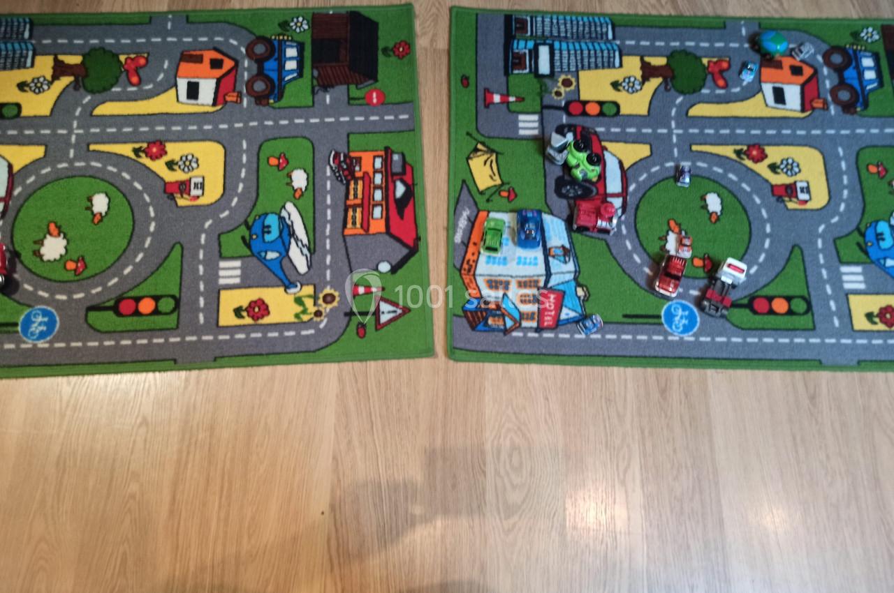 Deux tapis pour enfants avec des motifs de routes, véhicules et bâtiments, posés sur un sol en bois clair.