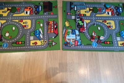 Deux tapis pour enfants avec des motifs de routes, véhicules et bâtiments, posés sur un sol en bois clair.