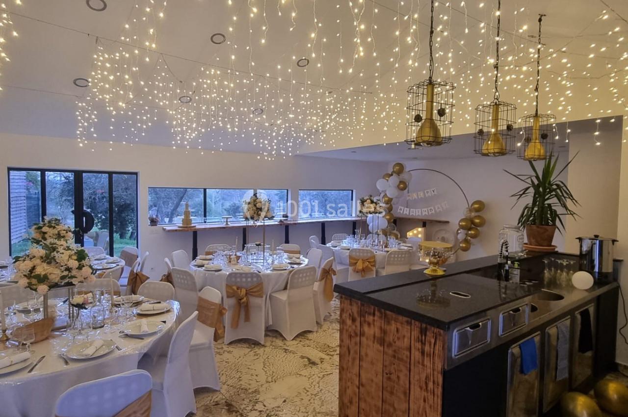 Salle décorée pour un événement, avec tables dressées, guirlandes lumineuses suspendues et ballons dorés.