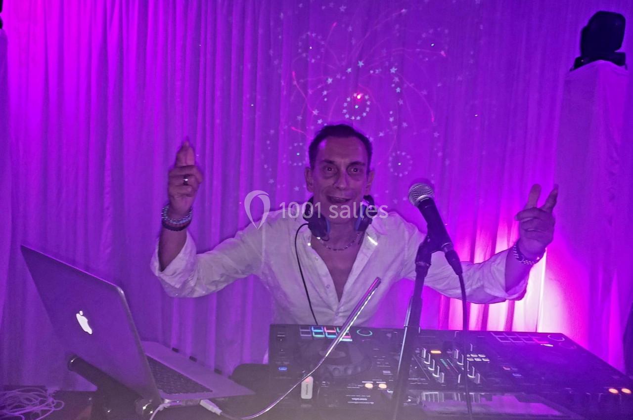 Un DJ en chemise blanche mixe de la musique sur une table de mixage, éclairé par des lumières violettes.