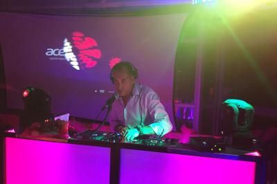 Table de mixage avec platines, microphones et panneau lumineux indiquant ’DJ Olivier’ sur une table en bois.