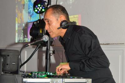 Table de mixage avec platines, microphones et panneau lumineux indiquant ’DJ Olivier’ sur une table en bois.