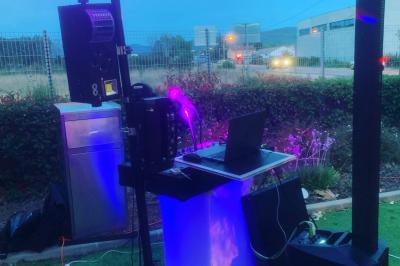 Table de mixage avec platines, microphones et panneau lumineux indiquant ’DJ Olivier’ sur une table en bois.