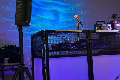 Table de mixage avec platines, microphones et panneau lumineux indiquant ’DJ Olivier’ sur une table en bois.