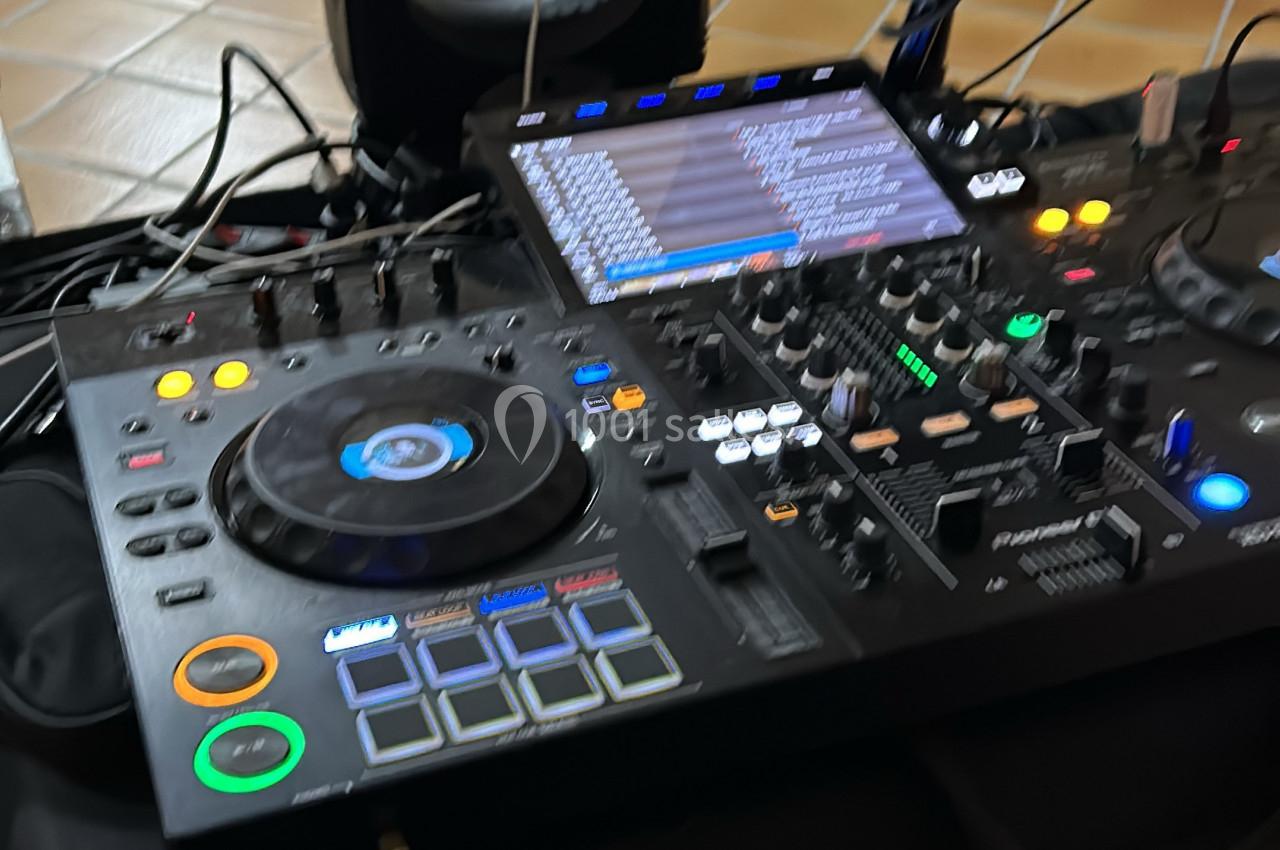 Table de mixage DJ avec platines, écran de contrôle et divers boutons lumineux, connectée à plusieurs câbles.