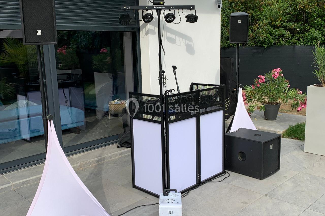 Matériel de sonorisation et éclairage installé en extérieur près d'une maison avec jardin en arrière-plan.
