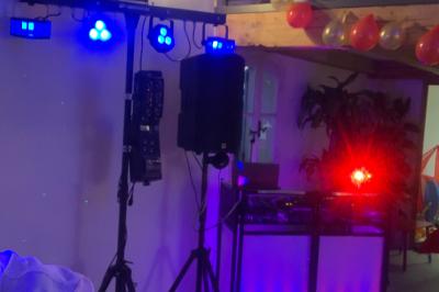 Table de mixage avec platines, microphones et panneau lumineux indiquant ’DJ Olivier’ sur une table en bois.