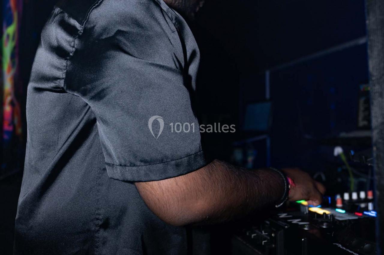 Un DJ en chemise noire manipule une table de mixage dans un environnement sombre.
