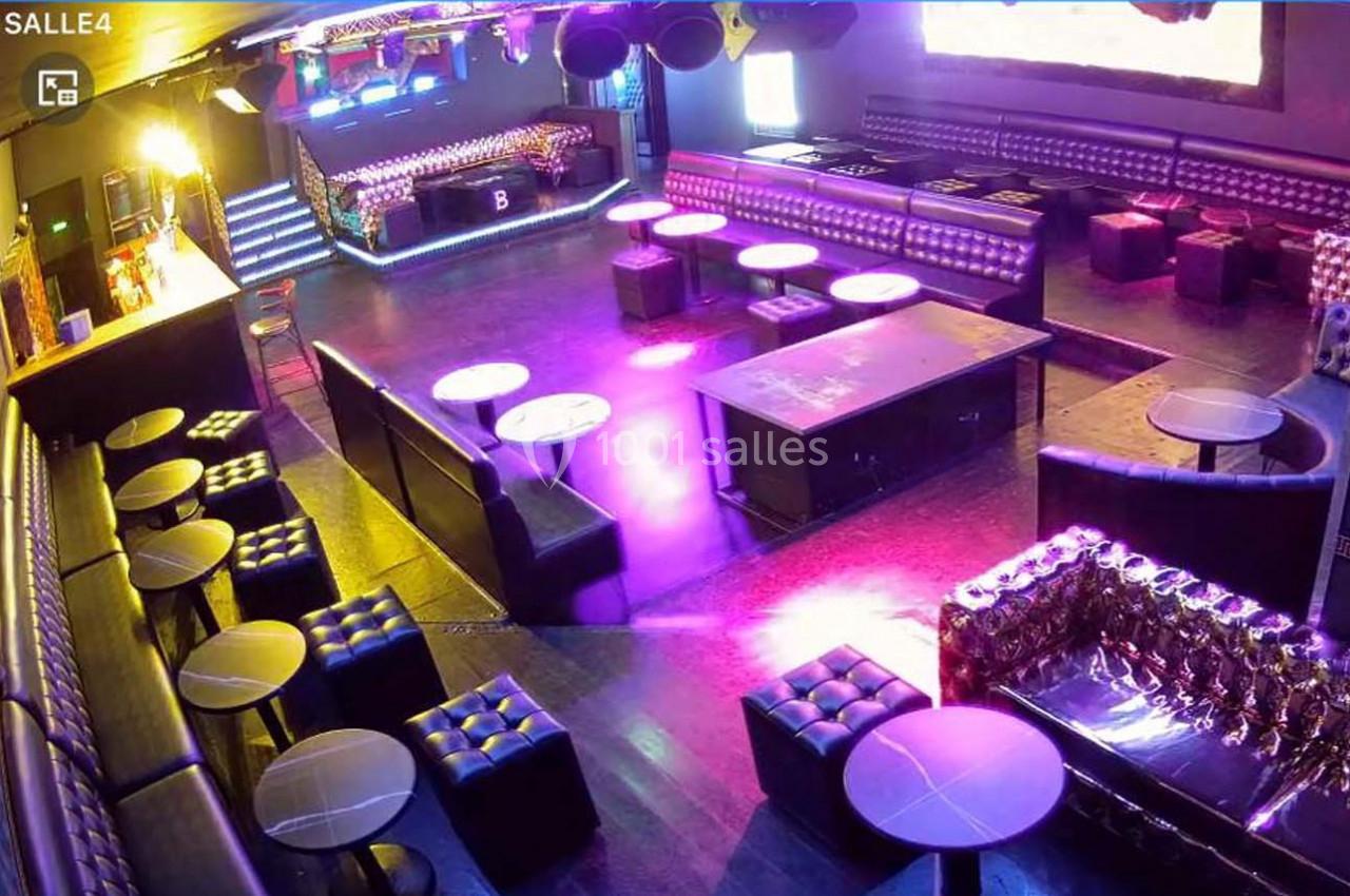 Salle de club vide avec banquettes, tables basses et éclairage coloré, vue d'ensemble de l'espace intérieur.