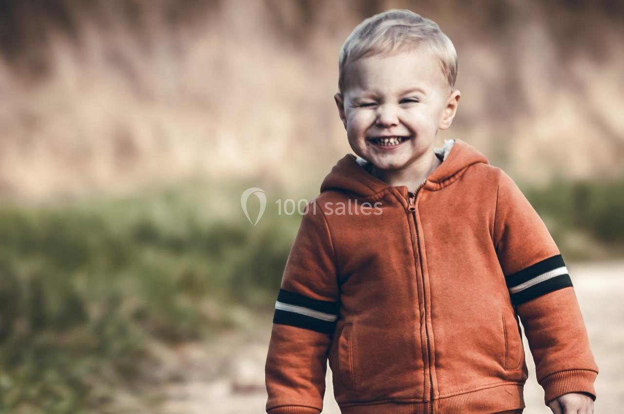 Un enfant souriant portant un sweat à capuche orange marche sur un chemin en plein air.